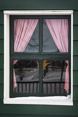 A window with red curtains that reflects the winter landscape. - 554673464