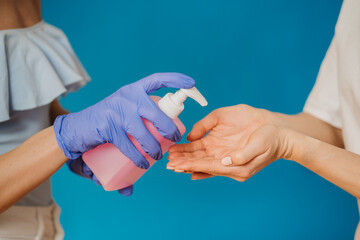Mother and daughter using wash hand sanitizer gel anti virus bacteria dirty skin care, close up hands over blue backdrop. Coronavirus pandemic concept.