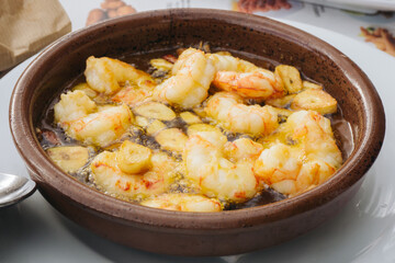 Shrimps in garlic dish. Restaurant meal in ceramic bowl. Seafood in olive oil. Spanish cuisine background.