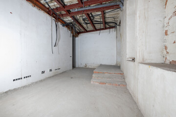 Raw room with plastered walls in renovated building with concrete floors, corrugated plastic pipes...