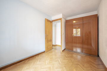 An empty room with a wardrobe with three-section glossy veneered doors with oak parquet floors...