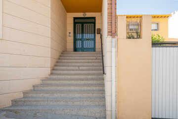 Entrance portal to a residential building with granite stairs, black metal railing and green painted front door