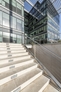 Image of a metal and glass facade with metal frames, railing with steel cables and white stone stairs of an office building