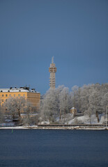 Fototapeta na wymiar Water front, frosty trees, old school, gazebo and tele tower a snowy blech winter day in Stockholm