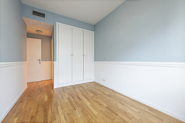 Blue walled room with a built-in wardrobe with three white lacquered doors with golden handles and oak wood floors