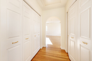 Dressing corridor of a bedroom with white lacquered wooden doors and a plaster arch on the wall