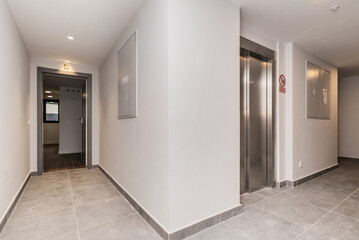 Portal of a house with white walls, gray floors and elevator with metal doors in stainless steel