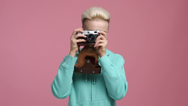 Portrait of a blonde-haired girl looking through the camera lens. Cheerful, smiling woman taking pictures in the studio. High quality 4k footage
