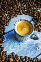 A pretty blue cup of freshly brewed espresso with foam and surrounded by fragrant roasted beans