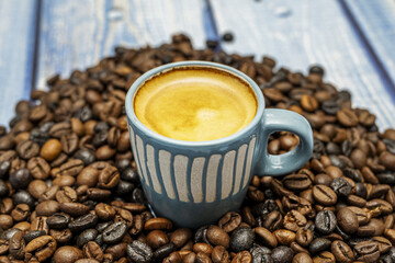 A pretty blue cup of freshly brewed espresso with foam and surrounded by fragrant roasted beans