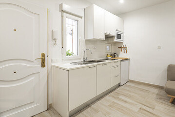 Small open kitchen in a living room of a studio with a small window and the white front door