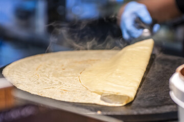 A chef cooking a large French crepe blowing smoke on a metal griddle