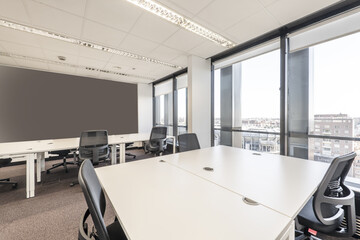 Office with several work tables and swivel chairs, gray walls, technical ceiling and large windows with a view