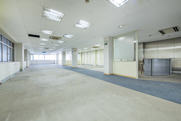 Spacious empty coworking office with gray walls, wooden shelves and glass partitions, a technical ceiling and a blue and gray carpet floor