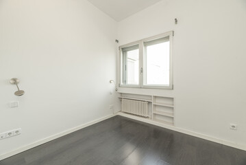 An empty room with a radiator and wooden shelves below a double aluminum window with gray floorboards
