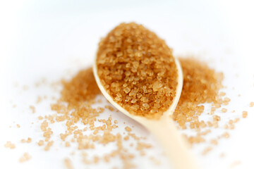 heap of brown sugar on plastic spoon, on white background