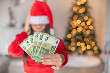 Frau mit Weihnachtsmütze und Geld als Geschenk in der Hand. Bokeh von den Lichtern eines...