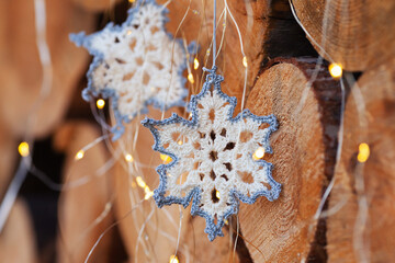 crocheted snowflakes decorations for the Christmas tree on the background of slices of large trees and bright led lanterns