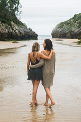 Two female hugging each other walking on the beach