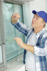 mature man installing roller shutter on window