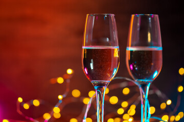 Two glasses of sparkling wine on a festive side garland background with colored light