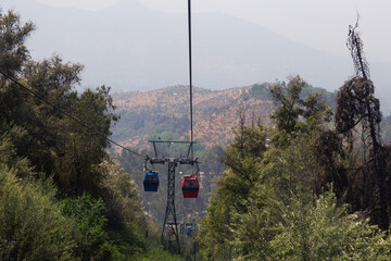 Red and blue cable car cabins moving along the Metropolitan Park of San Cristobal Hill, with hazy...