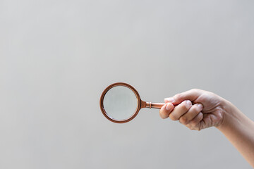 Find keywords concept. Woman holding magnifying glass on grey background, closeup. 