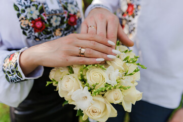 Obraz na płótnie Canvas Golden wedding rings on the hands of the newlyweds. Man and woman in national Ukrainian clothes. Bridal bouquet with white flowers