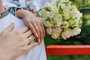 Obraz na płótnie Canvas Golden wedding rings on the hands of the newlyweds. Man and woman in national Ukrainian clothes. Bridal bouquet with white flowers