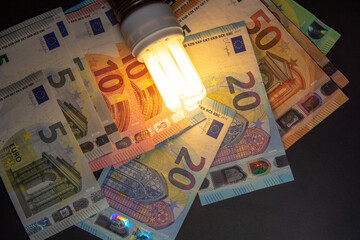 light from work light bulb and non -working lights on cash euro banknotes as price for electricity,...