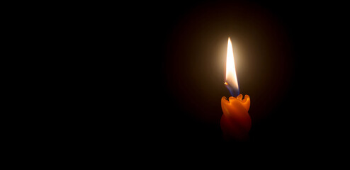 A single burning candle flame or light is glowing on a beautiful spiral orange candle on black or dark background with copy space for text on table in church for Christmas, funeral or memorial service