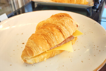 A piece of baked croissant ham cheese which is served in white dish. Bakery snack food object photo, close-up and selective focus.