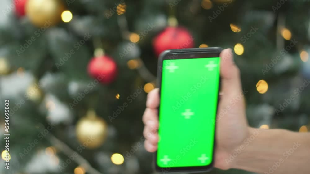 Poster human is holding a smartphone with a green screen on the background of christmas tree branches with 