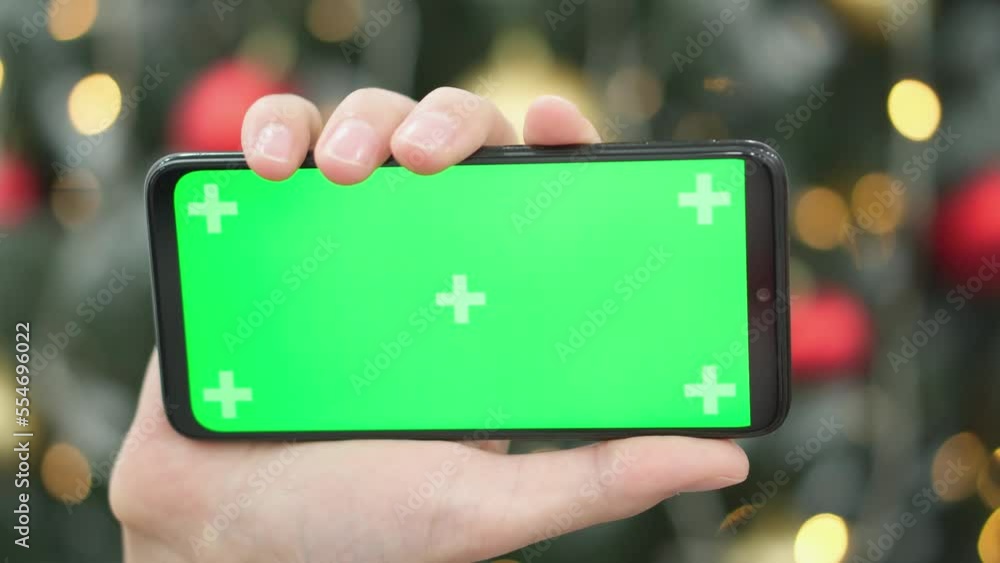 Poster human is holding a smartphone with a green screen on the background of christmas tree branches with 