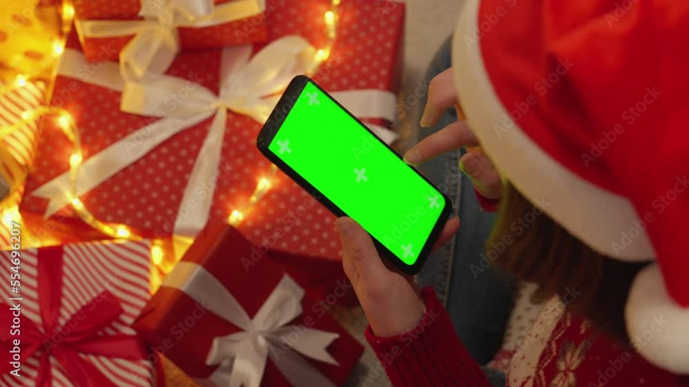 Poster human is holding a smartphone with a green screen on the background of christmas tree branches with 