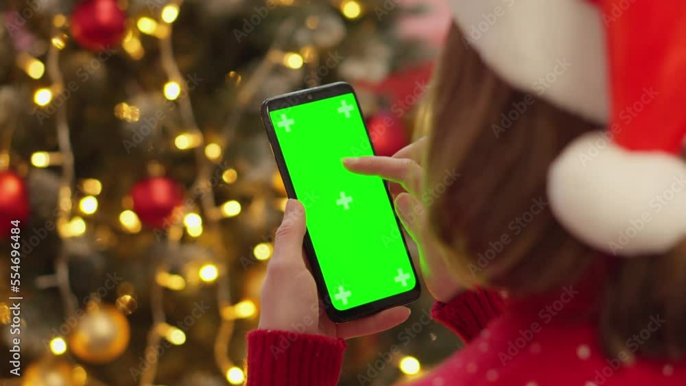 Poster human is holding a smartphone with a green screen on the background of christmas tree branches with 