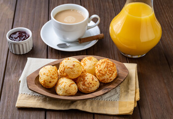 Typical brazilian cheese bun in a plate with coffee, butter and orange juice over wooden table
