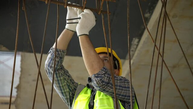 worker at a construction site is using a wire to bind rebar to form a plan for pouring cement.
