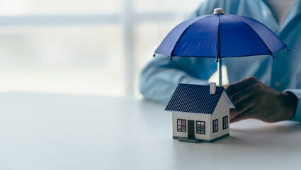 Businessman holding blue umbrella over model of wooden house real estate concept Insurance and...