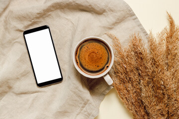 Mobile phone screen with mockup copy space and cup of coffee on linen towel with dry pampas grass....