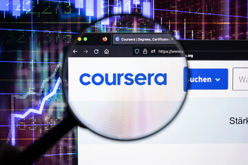 Coursera company logo on a website with blurry stock market developments in the background, seen on a computer screen through a magnifying glass