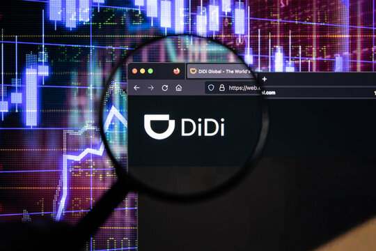 DiDi company logo on a website with blurry stock market developments in the background, seen on a computer screen through a magnifying glass
