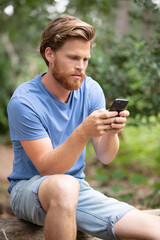 attractive young man sitting in the park using mobile phone