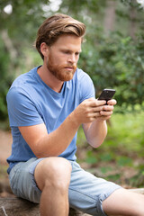 Fototapeta premium attractive young man sitting in the park using mobile phone