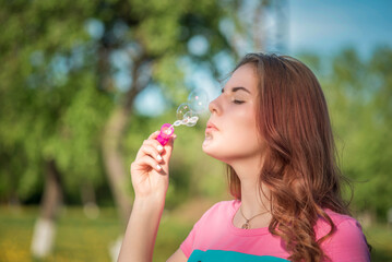 A young beautiful girl blows soap bubbles in a summer park.