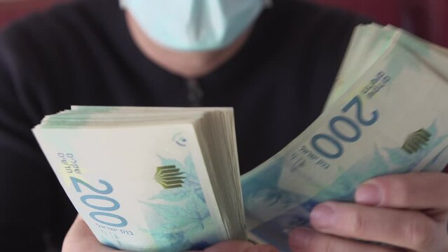 Counting cash Sheqel Israel currency paper 200 shekel nominal banknotes. Closeup of israeli man in face mask