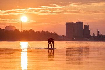 Silhouette of a woman paddle on an inflatable SUP board at sunrise and paddling through the shiny...