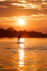 Silhouette of a woman paddle on an inflatable SUP board at sunrise and paddling through the shiny water surface of river