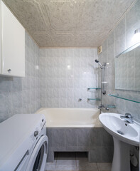 Simple bathroom interior in modern apartment. WHite sink, bath and tile. Washing machine