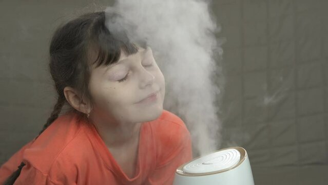 Childhood care with humidifier. A healthy little girl relax and breath with steam from air humidifier in the room.